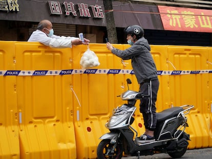 Un hombre entrega comida a otro a través del muro que separa las dos mitades de Shanghái a causa del confinamiento.