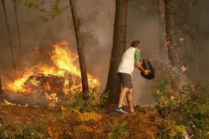 Una persona llança aigua en l'incendi a la zona de Zamanes, Vigo.