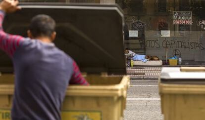 Un hombre busca en la basura delante de un mendigo que vive en la calle.
