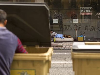 Un hombre busca en la basura delante de un mendigo que vive en la calle.