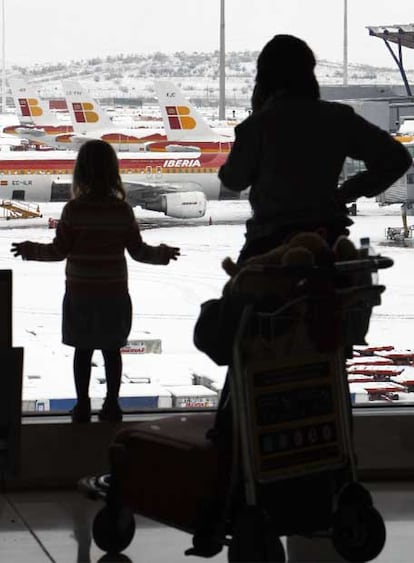 Los viajeros observan los aviones paralizados y cubiertos de nieve en el aeropuerto de Barajas.