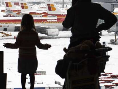 Los viajeros observan los aviones paralizados y cubiertos de nieve en el aeropuerto de Barajas.