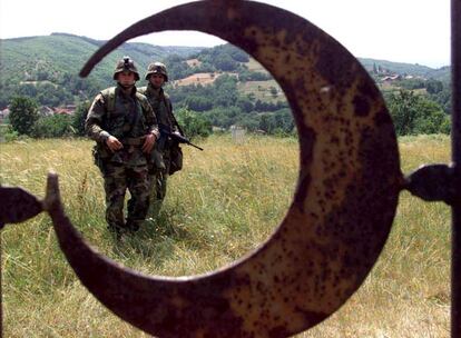 Dos soldados norteamericanos pasan junto a la puerta de un cementerio musulmán en Kacanik, donde desués de la guerra de Kosovo se descubrió una fosa común de decenas de cuidadanos albano-kosovares desaparecidos, presuntamente asesinados durante la limpieza étnica serbia