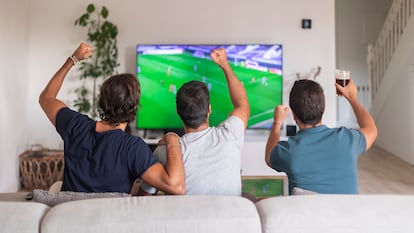 Tres amigos sentados en un sofá viendo un partido en la TV.