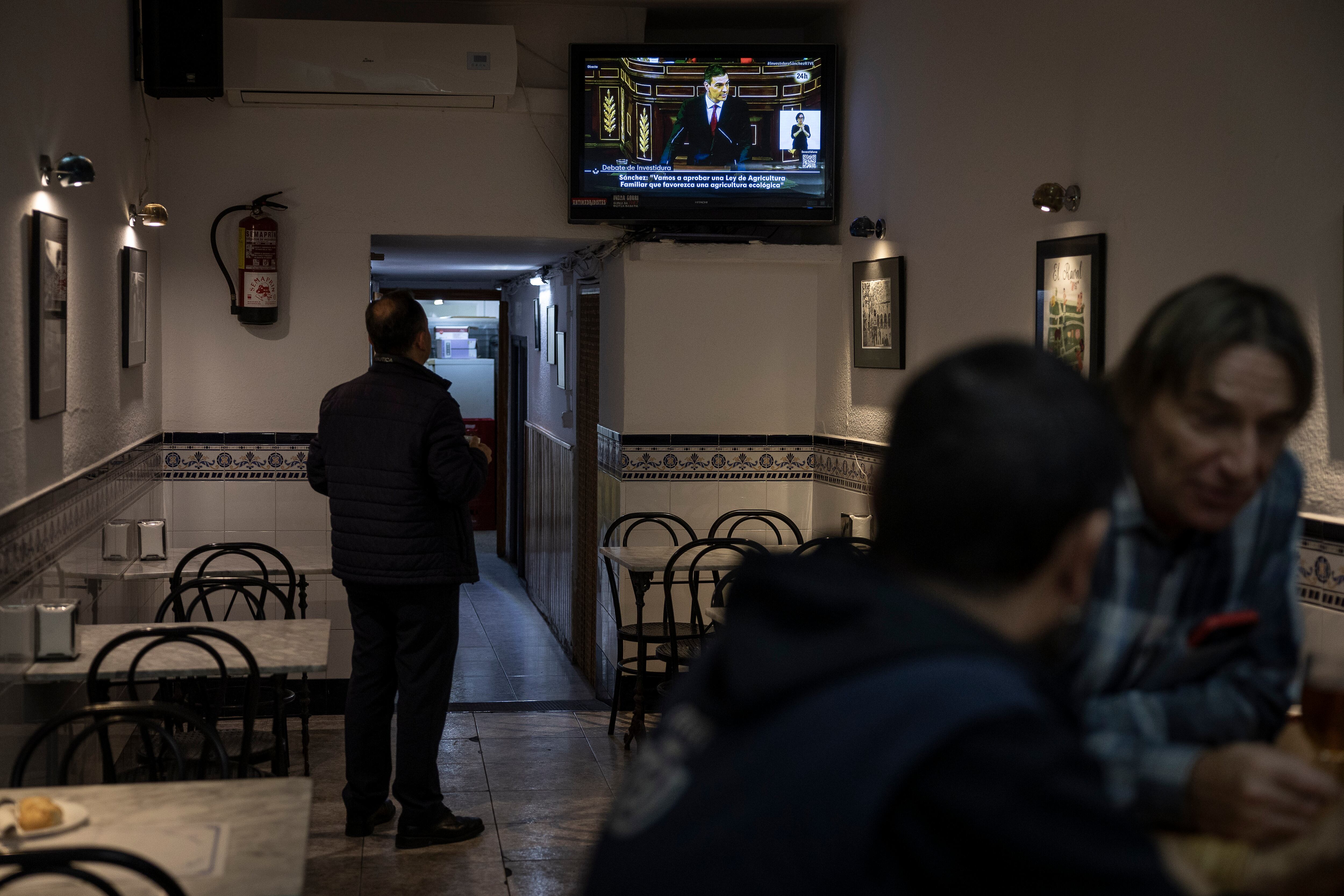 Clientes de un bar del centro de Barcelona siguen el discurso de investidura de Pedro Sanchez. 