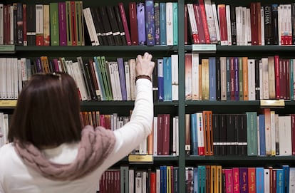 Una mujer coge un libro de una estanter&iacute;a.