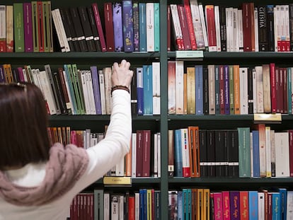 Una mujer coge un libro de una estanter&iacute;a.