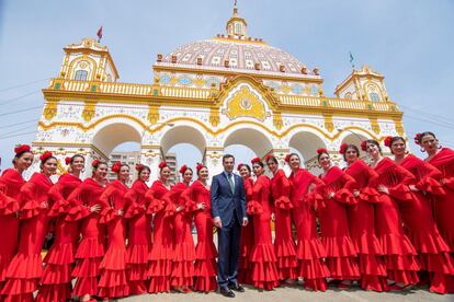 El presidente de la Junta de Andalucía, Juanma Moreno, posa con un grupo de mujeres vestidas de flamenca ante la portada del Real de la Fería de Abril de Sevilla.