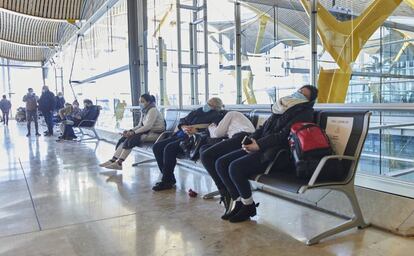 Varios pasajeros esperan sentados en los asientos de la Terminal 4.