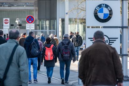 Trabajador pasan cerca del logotipo del fabricante alemán de automóviles BMW, en la planta de la misma empresa en Bavaria, el pasado 18 de marzo.