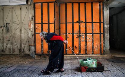 Una anciana tira de un carrito de cartón improvisado frente a una tienda cerrada en Jerusalén (Israel).