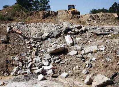 Una excavadora tapa con tierra parte de los escombros arrojados en un humedal cerca del río Miño.