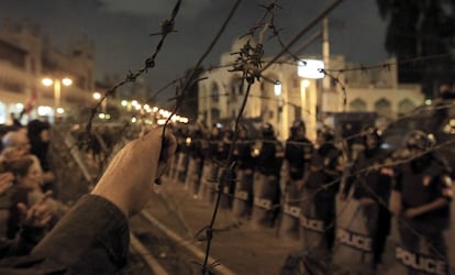 Un manifestante se agarra a una alambrada de espino con el Palacio Presidencial al fondo.