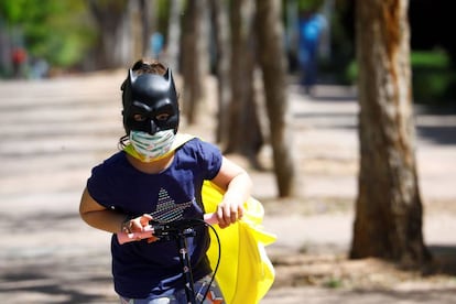 Una niña protegida con mascarilla y una careta de Batman juega con su patinete en la calle. 