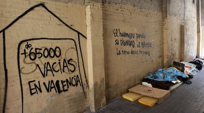 Varias personas duermen en la calle en el centro de Valencia junto a una pintada con el n&uacute;mero de casas vac&iacute;as.