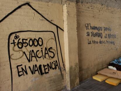 Varias personas duermen en la calle en el centro de Valencia junto a una pintada con el n&uacute;mero de casas vac&iacute;as.