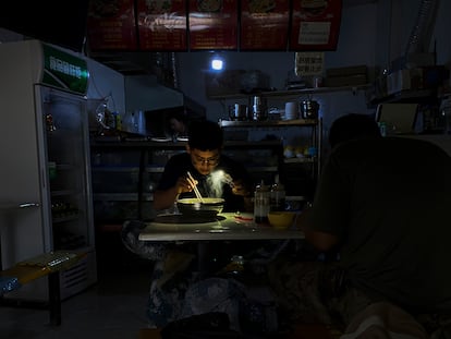 Un hombre utiliza la luz de su móvil para ver mientras desayuna durante un apagón en la ciudad de Shenyang, en el noreste de China