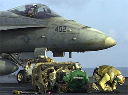 Dos técnicos militares preparan el despegue de un caza F-18 en el portaaviones <i>USS Enterprise,</i> en el mar Arábigo.