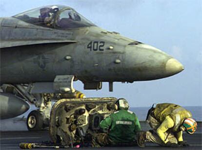 Dos técnicos militares preparan el despegue de un caza F-18 en el portaaviones <i>USS Enterprise,</i> en el mar Arábigo.