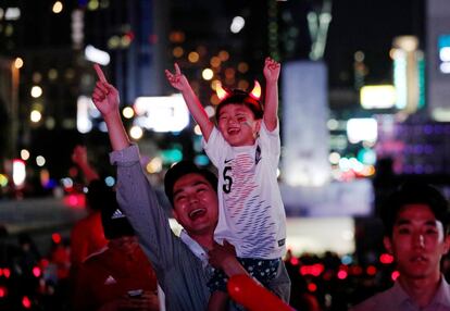 Un hombre coge en brazos a su hijo mientras ve la transmisión del partido de fútbol del Grupo F de la Copa Mundial entre Suecia y Corea del Sur, en el centro de Seúl, Corea del Sur.