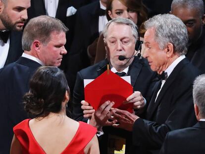 Brian Cullinan (à esquerda e com expressão séria), da PriceWaterHouseCoopers, fala com Warren Beatty no palco. De costas, de vestido vermelho, a outra auditora da PWC, Martha Ruiz.