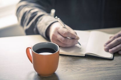 Una persona escribiendo en un cuaderno. 