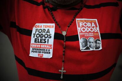 O propósito do protesto é reforçar a luta pela saída de Temer e o pedido de eleições diretas. Um manifestante com um terço e dois adesivos contra o presidente Temer, nos protestos de Brasília.