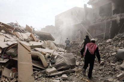Ciudadanos caminan entre los escombros tras un ataque aéreo en Saqba (Siria).