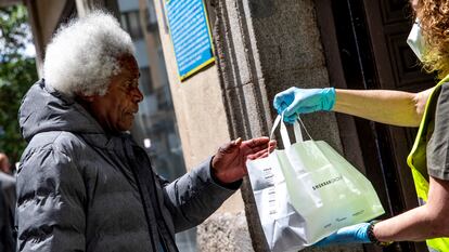 Una voluntaria de Mensajeros de la Paz entrega una bolsa con comida a una persona que ha quedado en situación vulnerable a causa del impacto de la covid-19 en Madrid, en mayo de 2020.