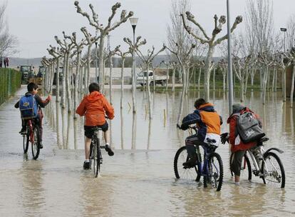 Varios niños montan en bicicleta en una zona próxima a las piscinas municipales de la localidad navarra de Falces, inundada a causa del desbordamiento del río Arga por las intensas lluvias de las últimas horas.