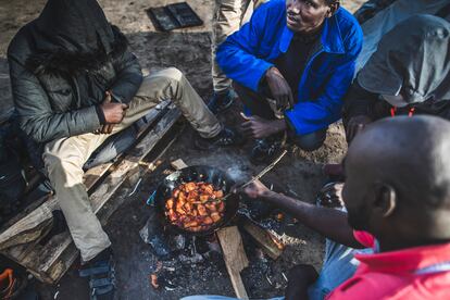 Un grupo de inmigrantes cocina y se calienta junto a un fuego en el campamento en el que aguardan para cruzar desde Calais, en Francia, hasta el Reino Unido