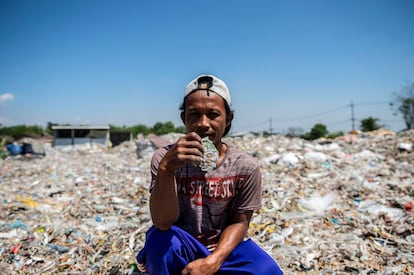 La represión de Indonesia a los desechos extranjeros importados ha trastornado la aldea de Bangun, donde los residentes dicen que ganan más dinero clasificando pilas de basura que cultivando arroz. En la imagen, Keman sentado entre los desechos plásticos en el pueblo de Bangun.