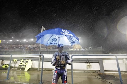 El piloto español de MotoGP, Jorge Lorenzo, camina bajo la fuerte lluvia protegido por un paraguas, tras el aplazamiento del Gran Premio de Qatar de MotoGP de motociclismo, en el circuito internacional de Losail.