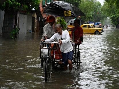 Varias personas caminan en un carro por una calle inundada tras la llegada del ciclón Remal el 27 de mayo en Calcuta, India.