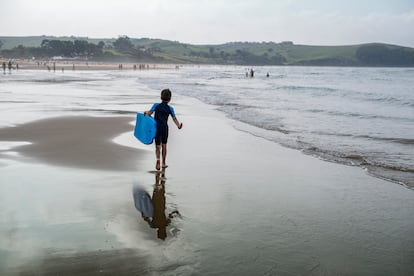 Un niño con su traje de neopreno y su tabla de surf caminando por la playa de Oyambre, en Cantabria.