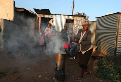 Una mujer prepara un brasero frente a una peluquería improvisada, durante los cortes de electricidad en Soweto, Sudáfrica, 19 de junio de 2020. 