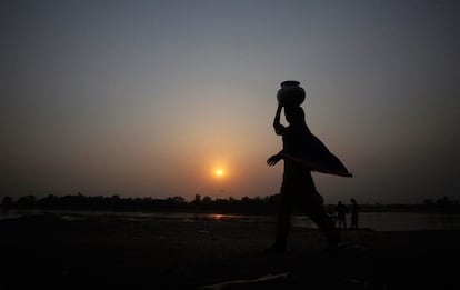 Una mujer traslada en su cabeza una vasija de agua durante el atardecer en Lahore, Pakistán.