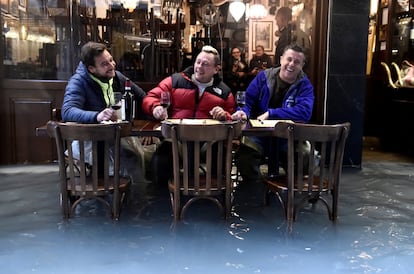 Tres hombres toman una copa de vino en una calle inundada en Venecia.   