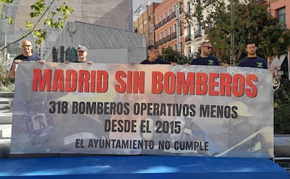 Cinco bomberos sostienen una pancarta frente al monumento en honor a los profesionales fallecidos en el incendio de Almacenes Arias en 1987, este miércoles en Madrid