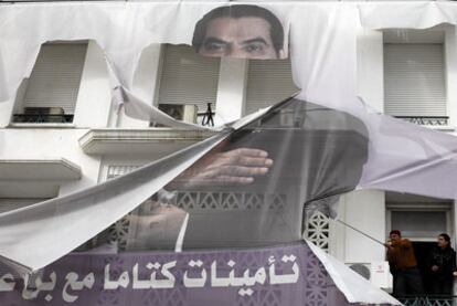 Un hombre intenta quitar desde un balcón un cartel gigante con la imagen del derrocado presidente de Túnez Ben Ali.