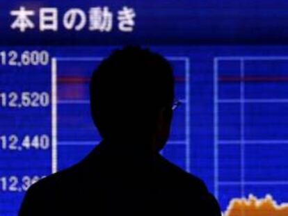 Peatones caminan junto a una pantalla informativa que muestra el índice de la bolsa en Tokio (Japón).