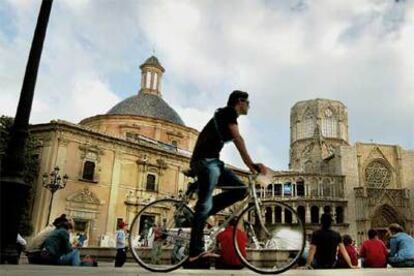 Paseantes y ciclistas disfrutando del aire libre en la plaza de la Virgen, en Valencia. A la izquierda, la catedral y su portada gótica, y a la derecha, la basílica de la Virgen de los Desamparados.