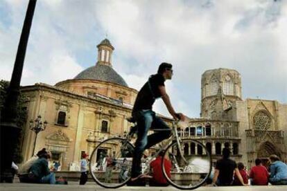 Paseantes y ciclistas disfrutando  del aire libre en la plaza de la Virgen, en  Valencia. A la izquierda, la catedral y su portada gótica, y a la derecha, la basílica de la Virgen de los Desamparados.