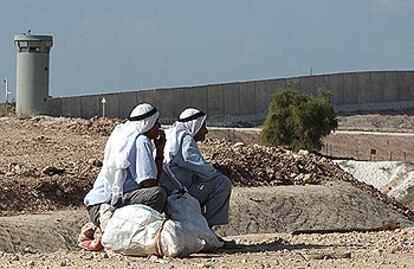Dos palestinos observan un control israelí ante el muro de separación levantado en Cisjordania.