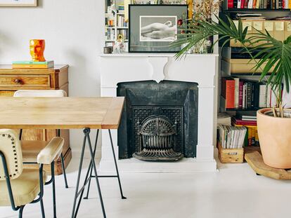 Salón de la casa con la chimenea y el suelo pintados de blanco para ordenar visualmente una estancia llena de volúmenes, libros y plantas. En la pared del fondo, la obra Luz sobre luz, de José María Sicilia. Debajo, el aparador de su abuela, un mueble del siglo XIX de origen piamontés.