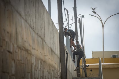 Dos jóvenes escalan el muro que protege el perímetro del puerto de Ceuta para acceder a la zona de seguridad. En el último mes, desde la crisis fronteriza, se han detectado incursiones casi diarias de personas que intentan abordar los barcos con destino a la Península escondidos en camiones o encaramados a los ferris.