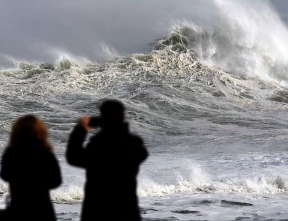 Dos persona fotografan el estado de la mar junto a la playa del Camello, Santander.