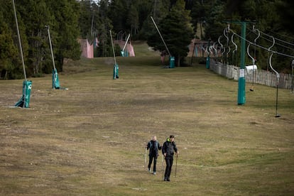 Dos excursionistas caminan por las pistas de esqui de La Masella (Girona), sin nieve, este sábado.