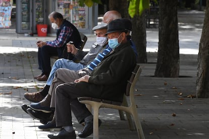 Varios vecinos descansan en un banco protegidos con mascarilla en León.