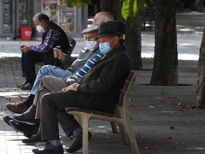 Varios vecinos descansan en un banco protegidos con mascarilla en León.